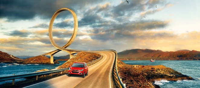 一台紅色的車子沿著河岸馳騁在公路上