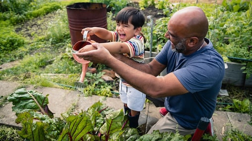 一名男子正在花園中幫一位孩子澆水