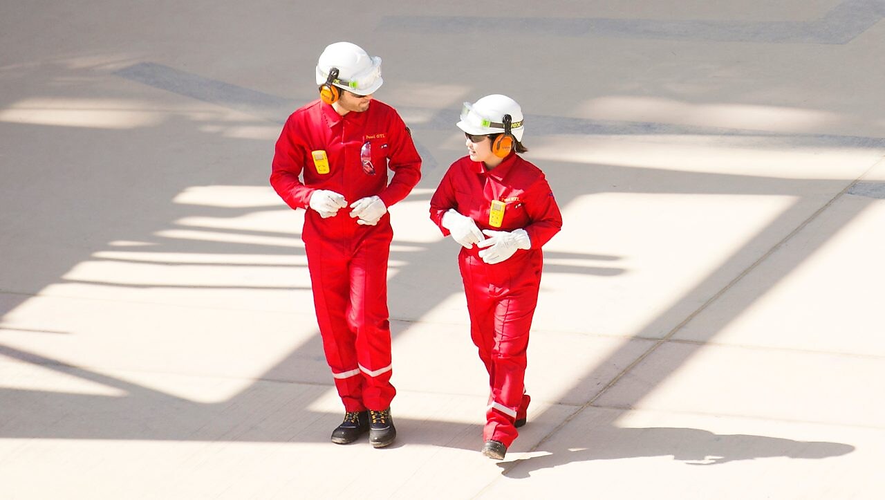 身穿紅色工作服、頭戴白色頭盔和聽力保護裝置行走的男女工人