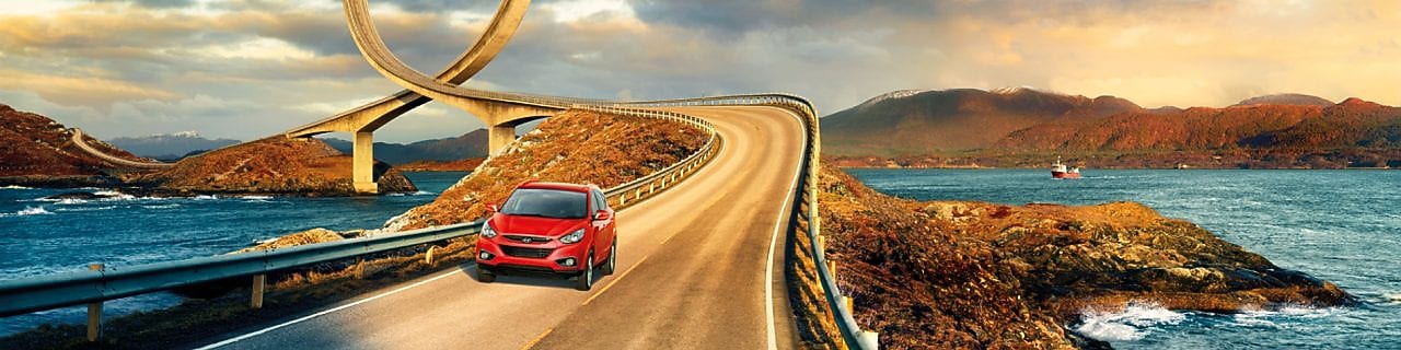 一台紅色的車子沿著河岸馳騁在公路上